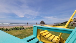 A view from a turquoise and yellow deck overlooking a beach with waves, a rock formation, and a distant hill. - Sea Sprite at Haystack Rock (Cannon Beach)