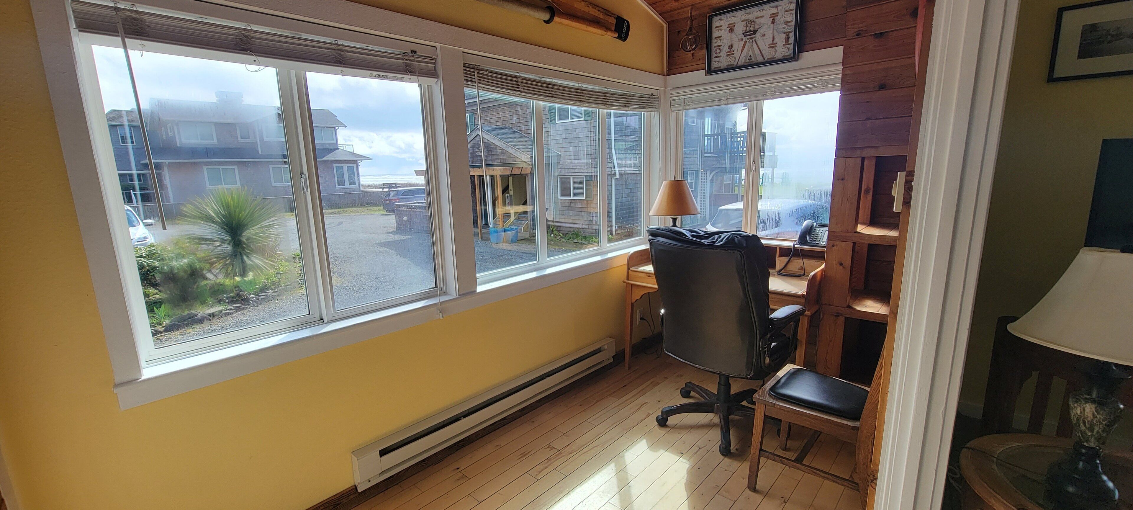 A room with large windows, a wooden floor, a desk with a chair, and a radiator.