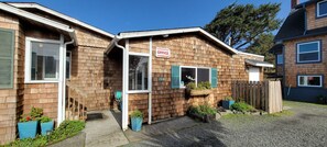 A wooden house with a 'For Sale' sign, a front door, and a small porch area.