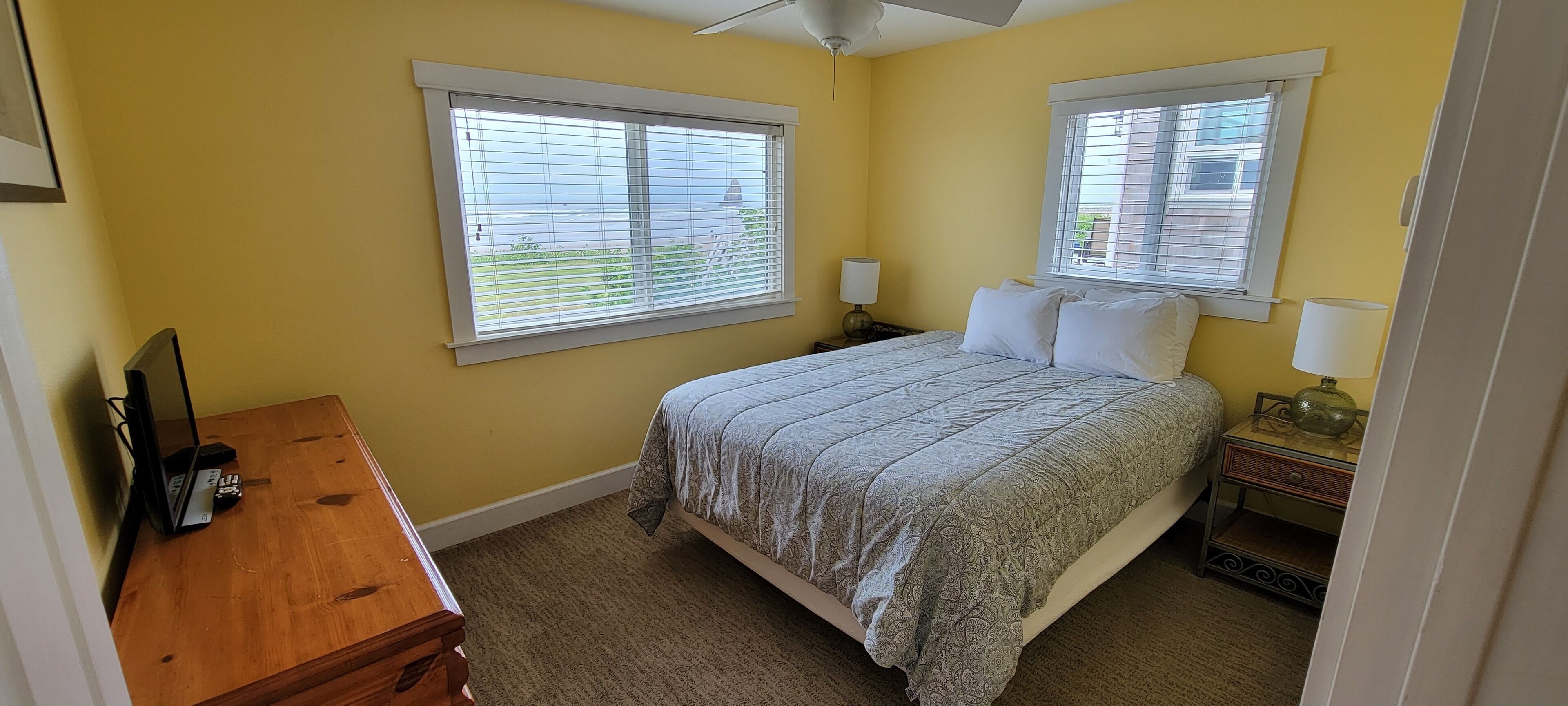 A bedroom with a bed, two bedside tables with lamps, a dresser, and a window with blinds.