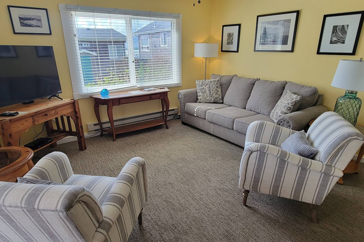 A living room with a TV, sofa, chairs, a coffee table, and a window with blinds.