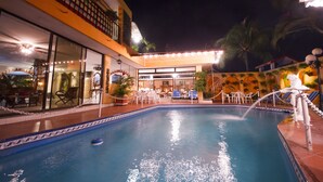 An indoor swimming pool with a tiled edge, surrounded by lounge chairs and a covered seating area. - Ideal Villa Hotel (Port-au-Prince)