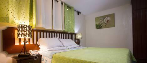 A neatly made bed with a green quilt, a bedside lamp, and a telephone on a wooden nightstand.