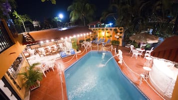 A swimming pool with lounge chairs and umbrellas, surrounded by a fence and potted plants.