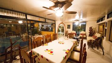 Comedor con una mesa grande, sillas, ventilador de techo y vistas a través de un ventanal.
