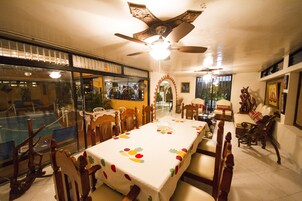Comedor con una mesa grande, sillas, ventilador de techo y vistas a través de un ventanal.