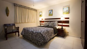 A bedroom with a zebra-patterned bedspread, a wooden bench, a nightstand with a lamp, and wall art depicting animals. - Ideal Villa Hotel (Port-au-Prince)