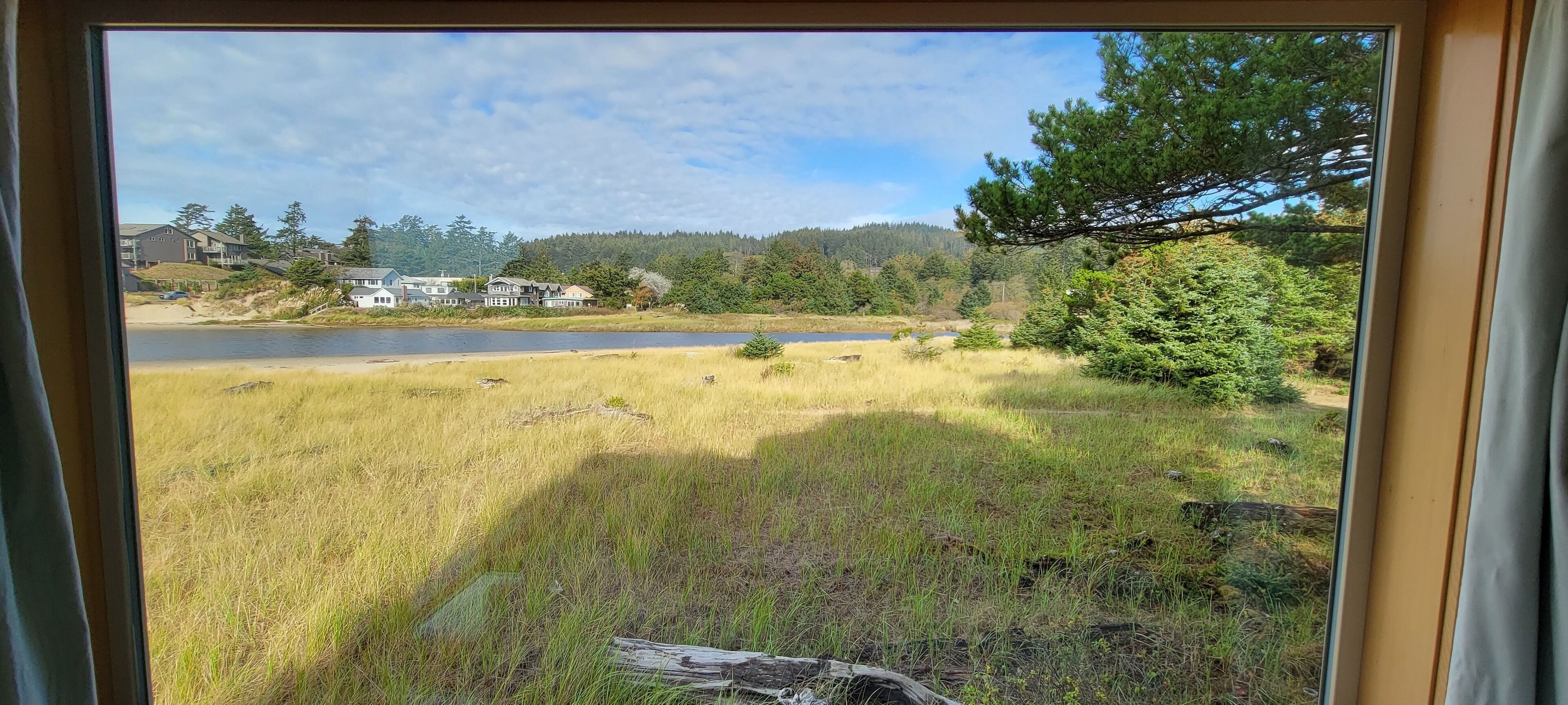 Blick auf ein grasbewachsenes Feld mit einem See und Häusern im Hintergrund.