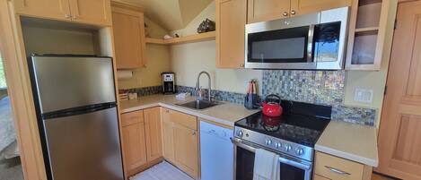 A compact kitchen with wooden cabinets, a stainless steel refrigerator, a microwave, a gas stove, and a dishwasher.