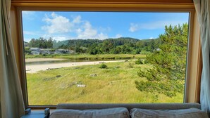 A room with a large window overlooking a grassy landscape with trees and a river. - Sea Sprite on the Estuary (Cannon Beach)