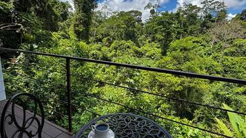 A balcony with two chairs and a table, each with a cup of coffee, overlooking a lush green forest.