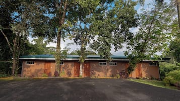 A two-story building with a green roof, surrounded by dense foliage.