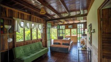 Un interior de madera con un sofá verde, paredes de madera y ventanas grandes.