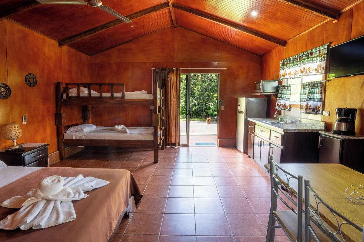 A wooden cabin-style room with two beds, a kitchenette, and a dining area.