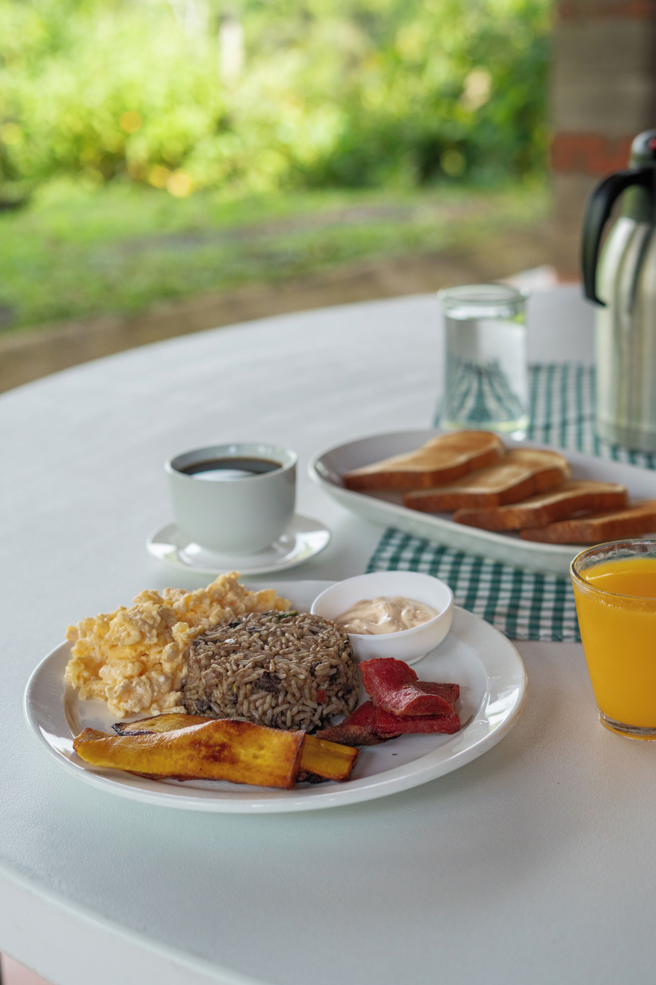 A breakfast plate with toast, scrambled eggs, black beans, and bacon, accompanied by a cup of coffee and a glass of orange juice on a table.