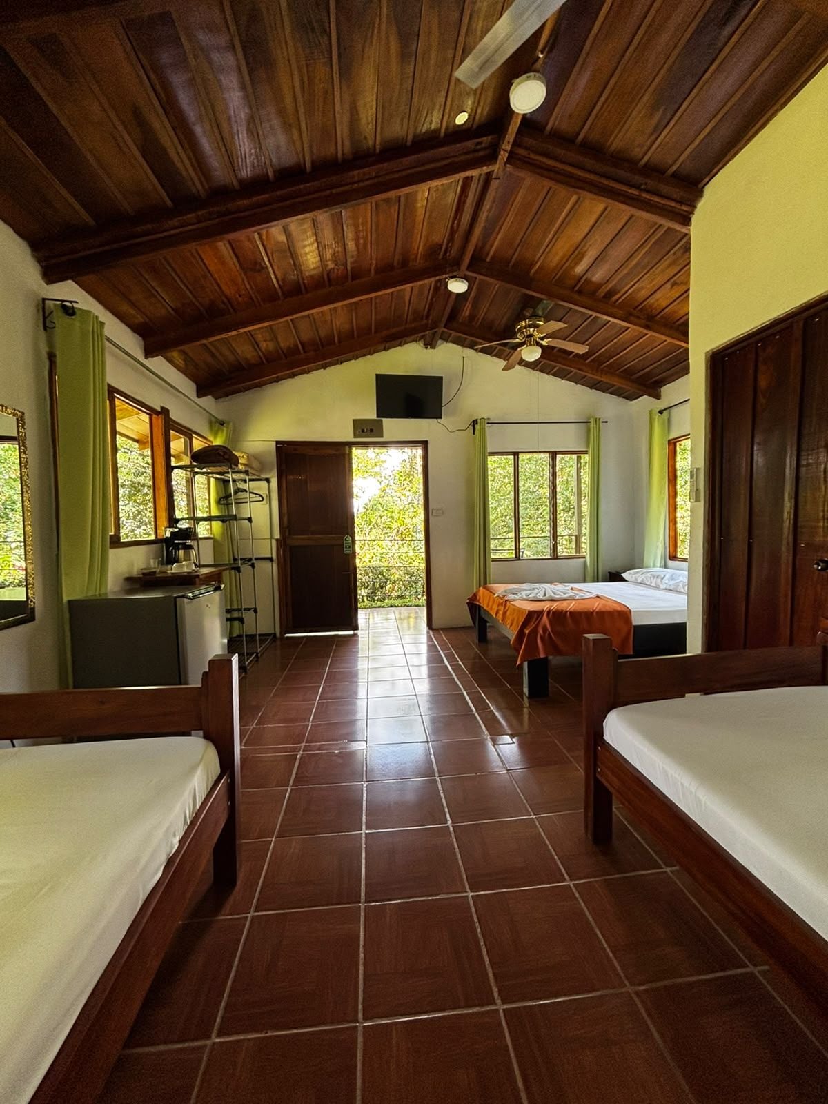 Una habitación con piso de madera, ventilador de techo y cama con cortina verde.