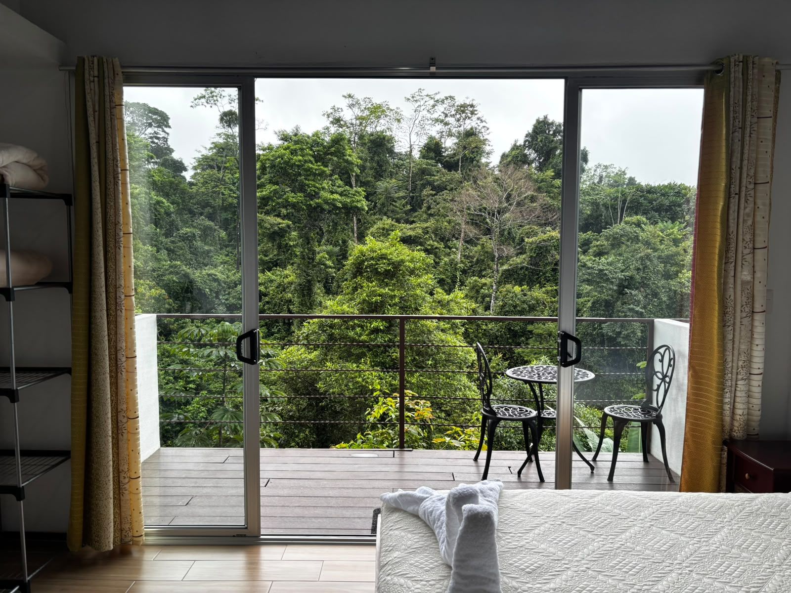 Un dormitorio con un amplio ventanal corredera que da a un balcón con vistas a una zona boscosa.