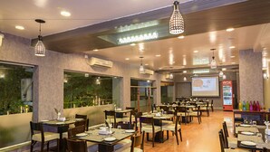A restaurant with multiple dining tables and chairs, large windows, and ceiling lights. - Inventree Hotel, Hinjewadi (Paud)