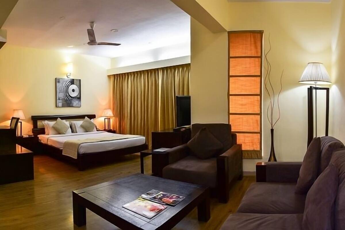 Una habitación de hotel con cama, sofá, mesa de centro, televisión y lámpara.