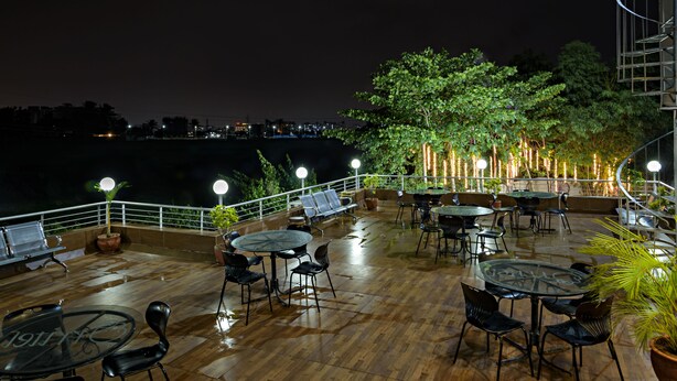 An outdoor patio area with tables and chairs, surrounded by potted plants and a railing. - Inventree Hotel, Hinjewadi (Paud)