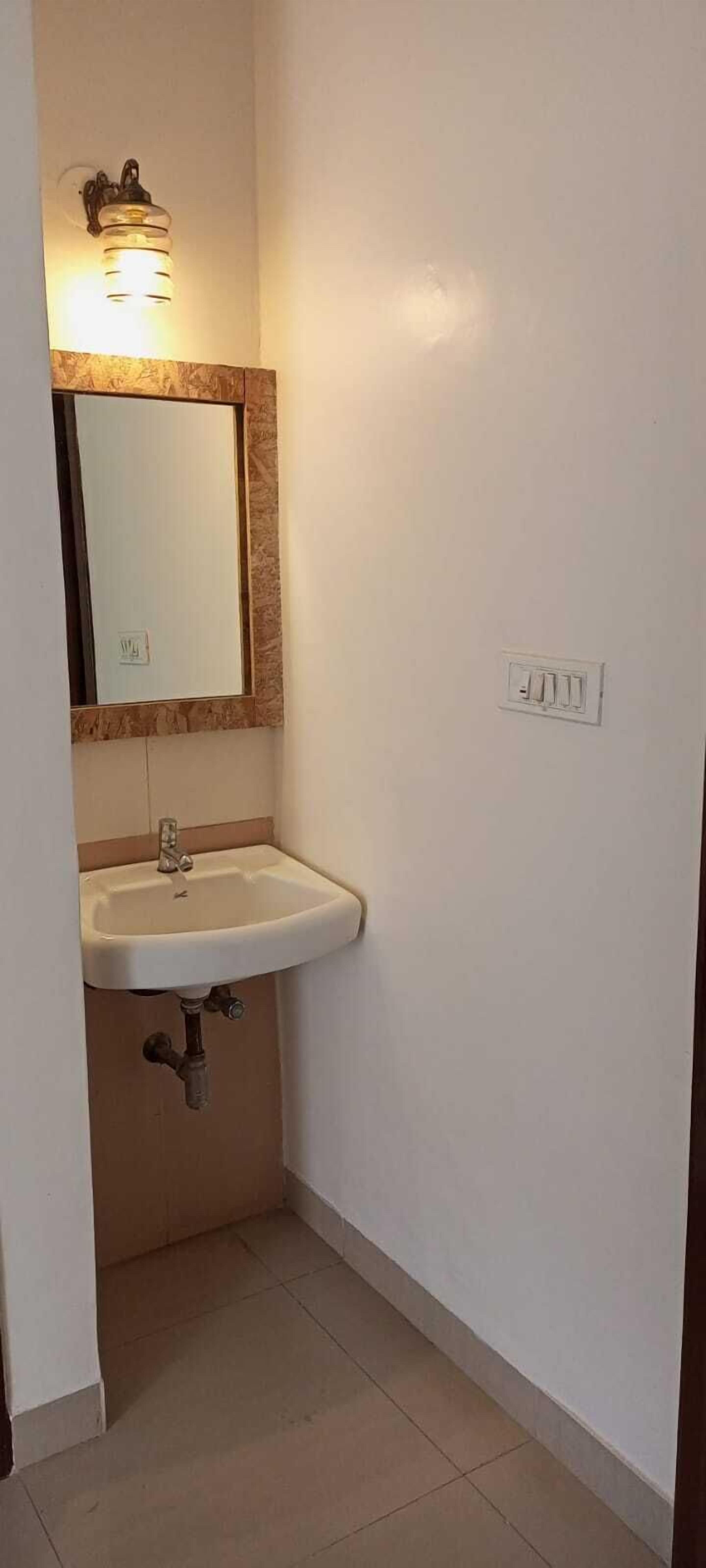 Une petite salle de bain avec un lavabo blanc, un miroir doté d’un cadre en bois et un luminaire placé au-dessus du miroir.
