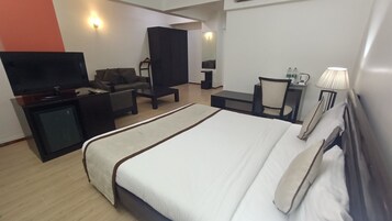 Una habitación de hotel con una cama, televisión, escritorio, silla y lámpara.