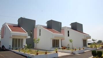 A modern building with a flat roof, white walls, and a red-tiled roof. There are potted plants in front of the building.