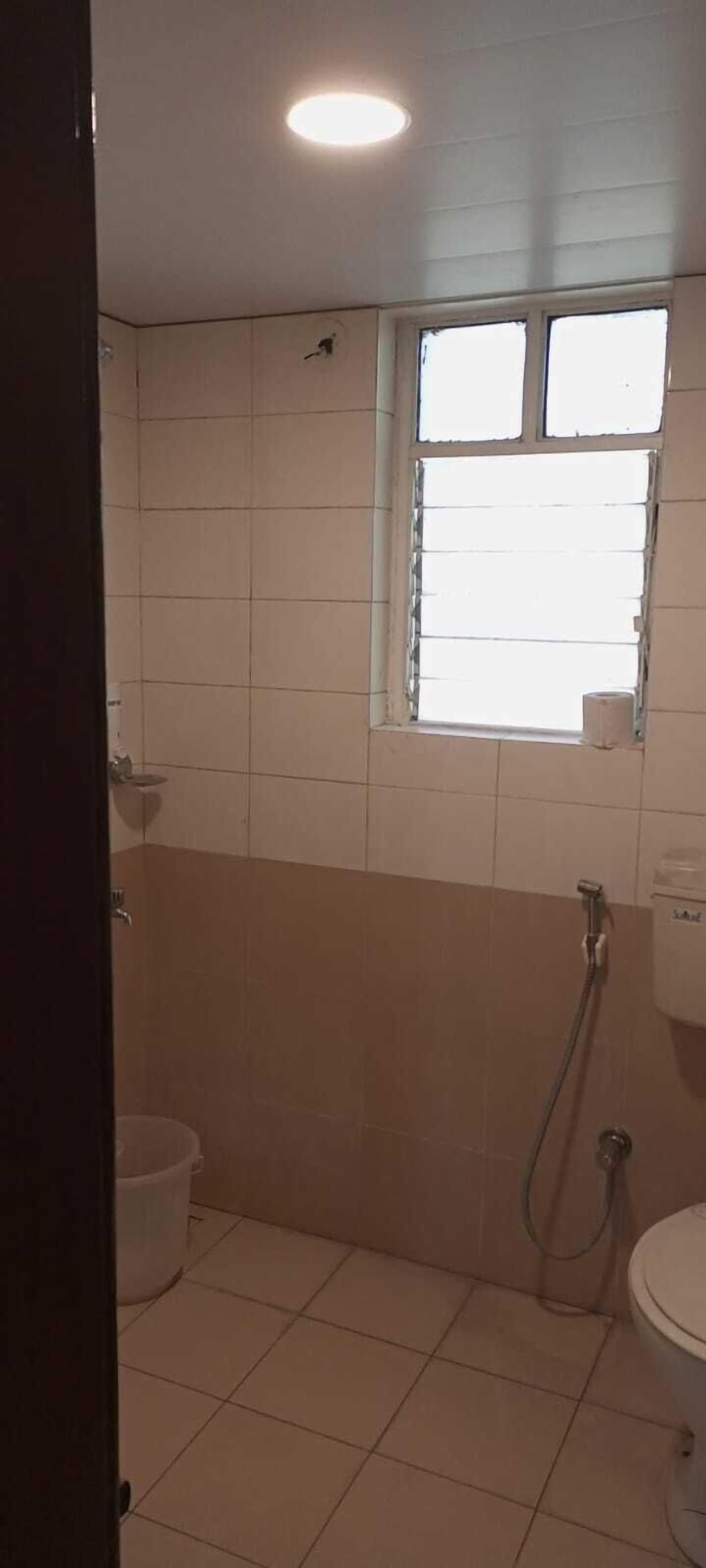 Casa de banho com azulejos brancos, janela, chuveiro e sanita.