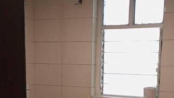 Casa de banho com azulejos brancos, janela, chuveiro e sanita.