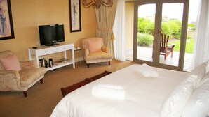 Une chambre d’hôtel avec un grand lit, un téléviseur posé sur une console blanche, un fauteuil à motifs floraux et une vue sur le jardin, visible à travers la porte-fenêtre coulissante.