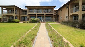 Un immeuble à plusieurs étages doté d’une cour intérieure, avec un chemin piétonnier dallé et une végétation luxuriante tout autour.