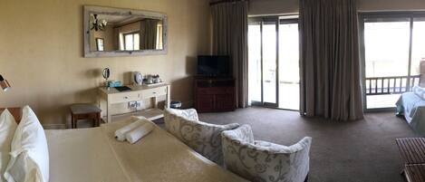 A hotel room with a bed, a desk with a mirror, a television, and a view of the outside through a sliding door.