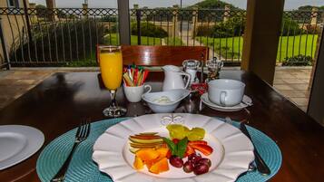 A breakfast table with a plate of fruit, a glass of orange juice, and breakfast items.