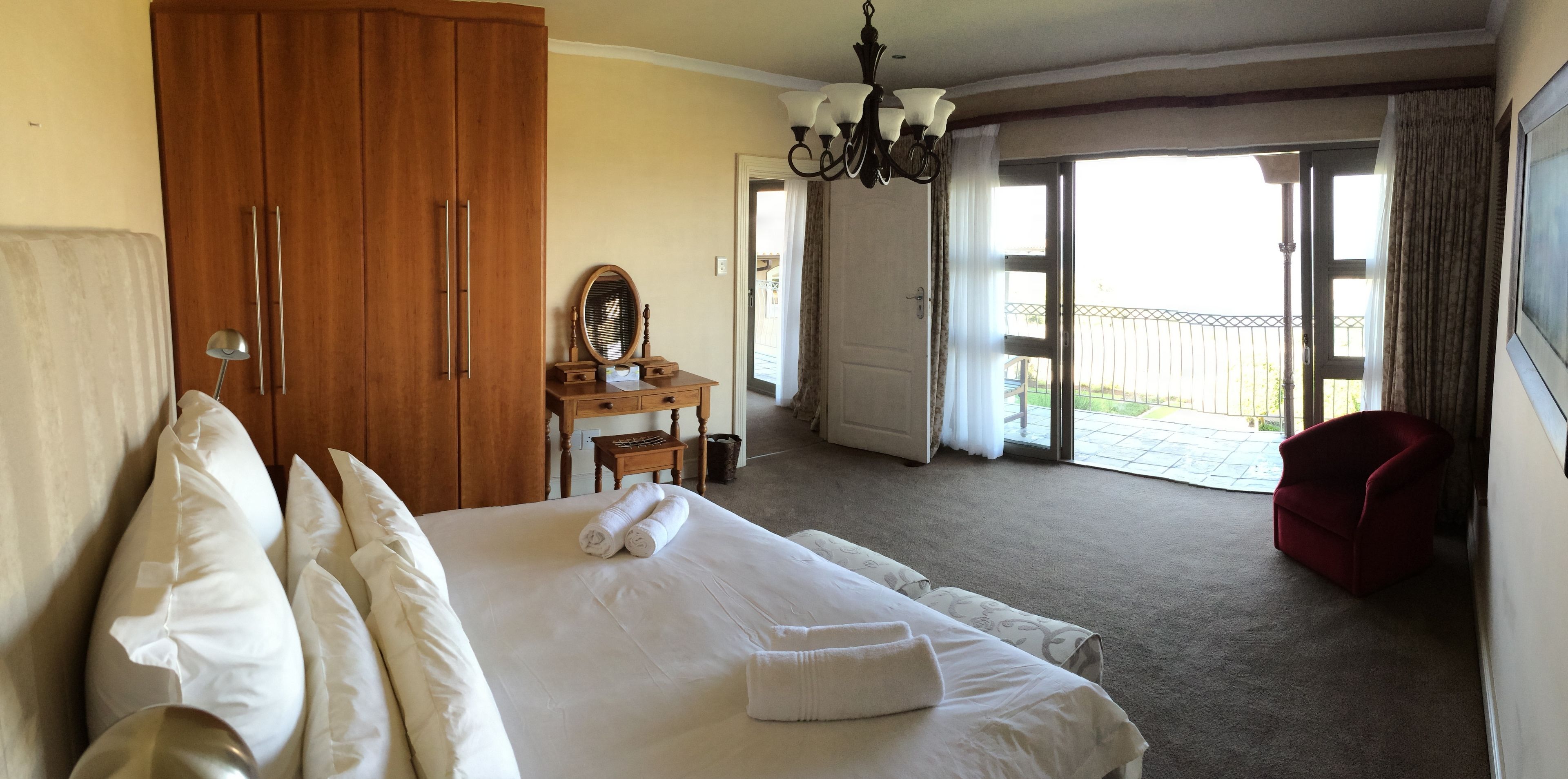 A hotel room with a large bed, a wooden wardrobe, a desk with a mirror, and a red armchair.