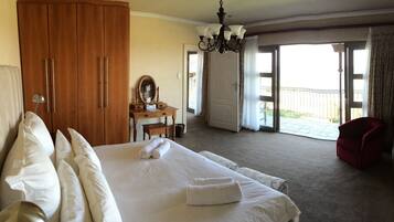 A hotel room with a large bed, a wooden wardrobe, a desk with a mirror, and a red armchair.
