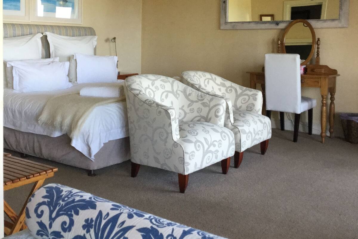 A bedroom with a bed, two armchairs, a desk, a mirror, and a chandelier.