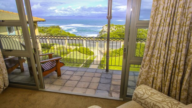 Un balcon avec vue sur l’océan, une chaise et un rideau à motifs.