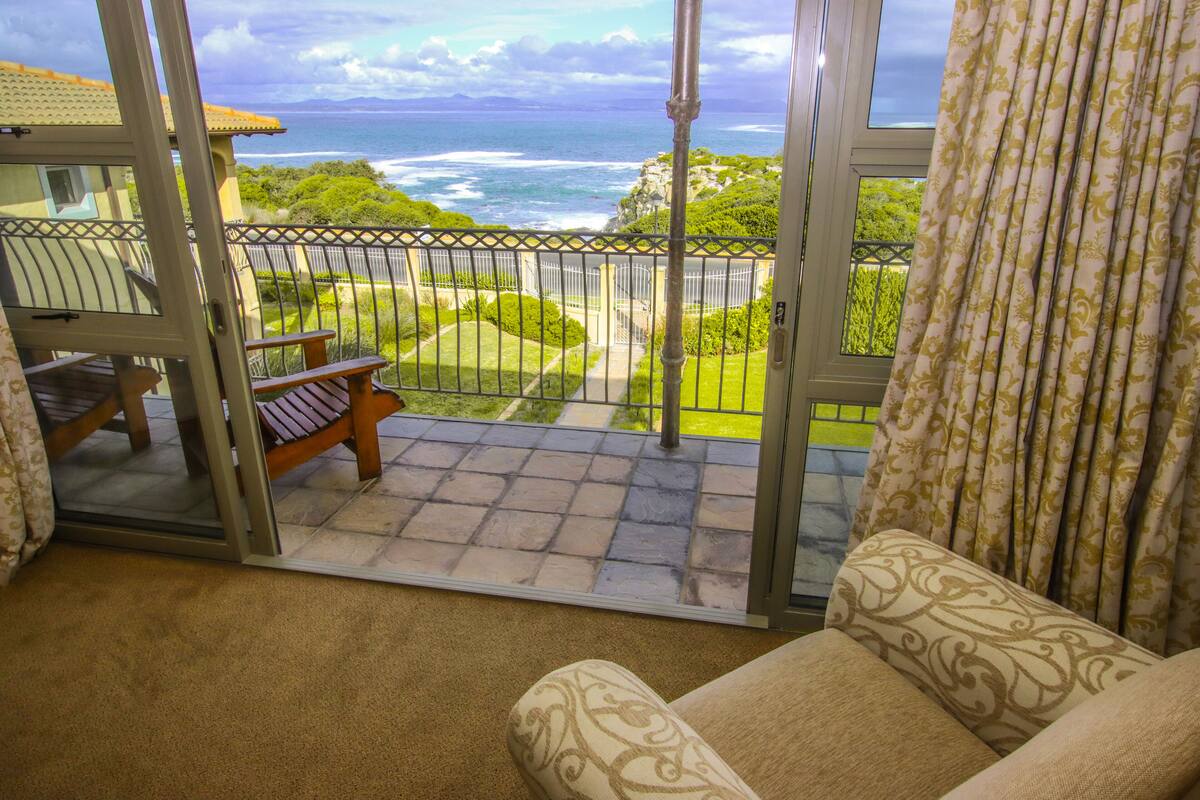 A balcony with a view of the ocean, a chair, and a patterned curtain.