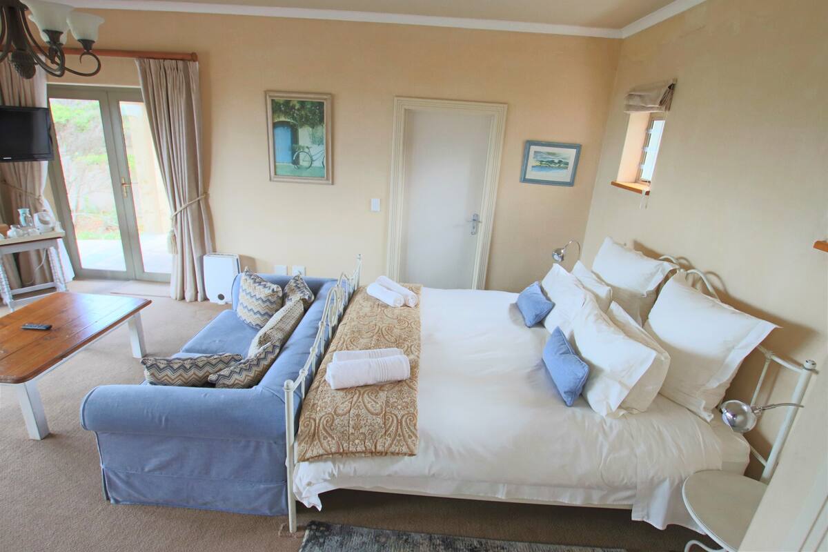 A hotel room with a bed, a sofa, a small table, and a television.
