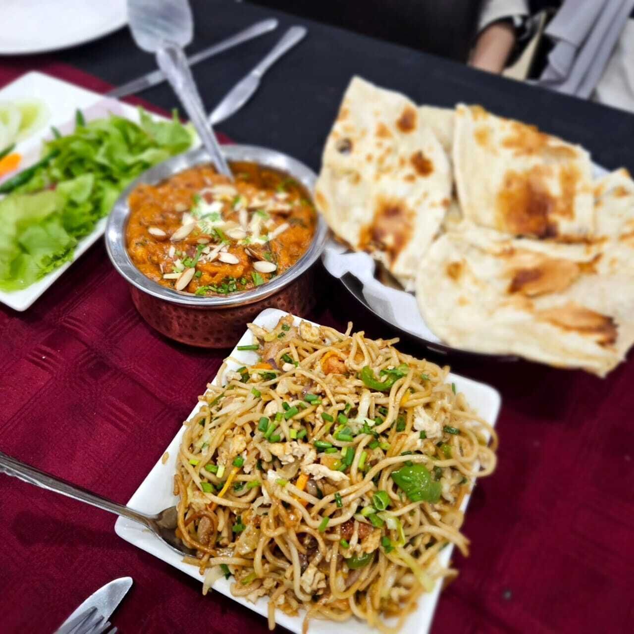 A table with a variety of dishes including noodles, a curry, and flatbreads.