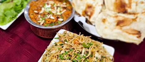 Una mesa con diversos platos, entre ellos fideos, curry y panes planos.