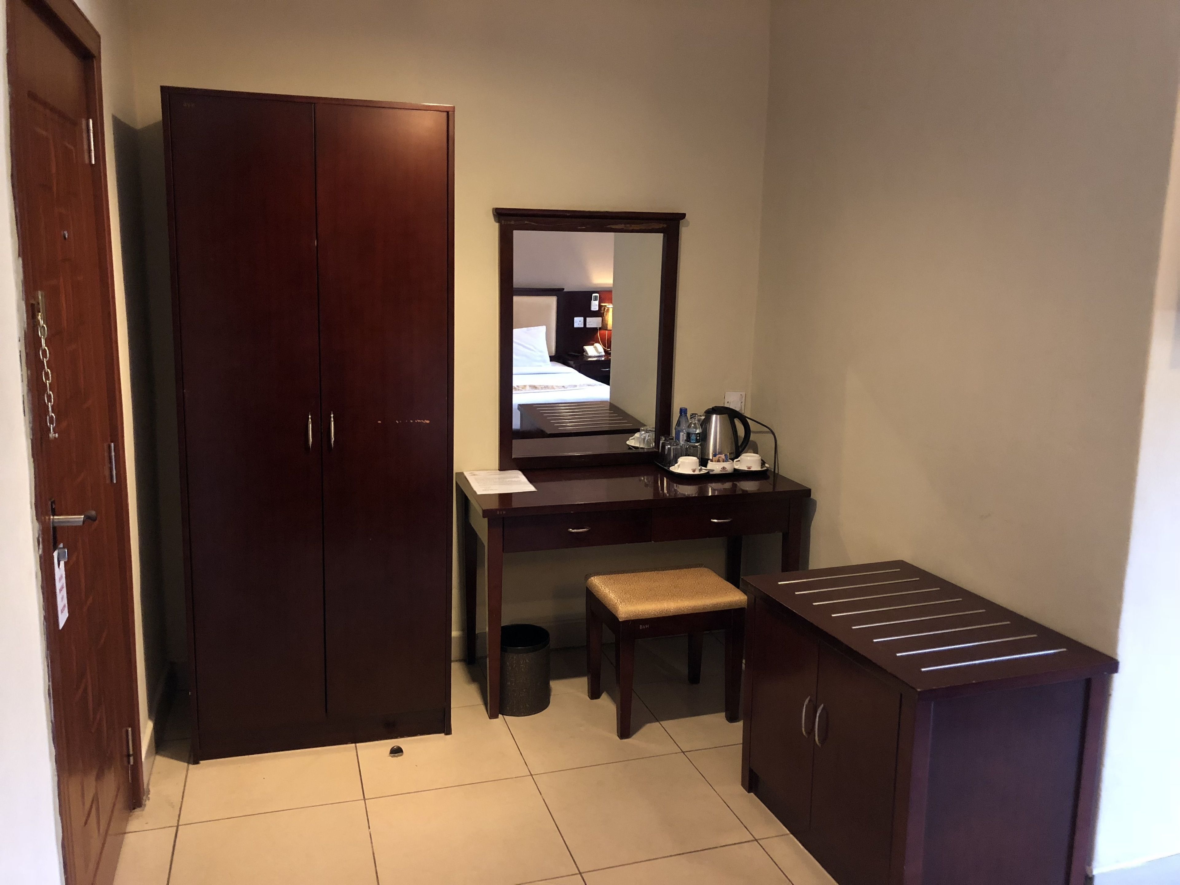 Una camera d'albergo con un'armadio in legno, una scrivania con uno specchio, una panca e una piccola credenza.
