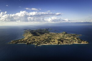 Vista aérea de una isla costera con vegetación verde y zonas arenosas, rodeada por el océano.