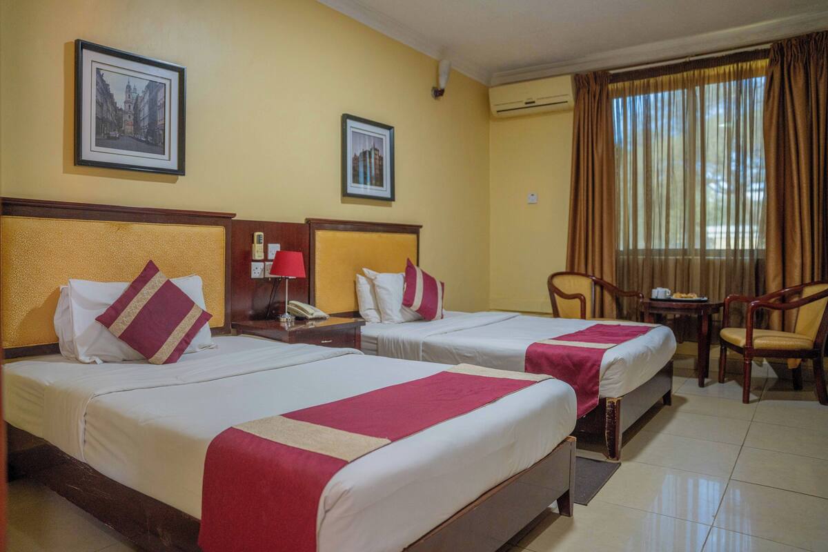 A hotel room with two beds, a desk, a chair, and a window with curtains.
