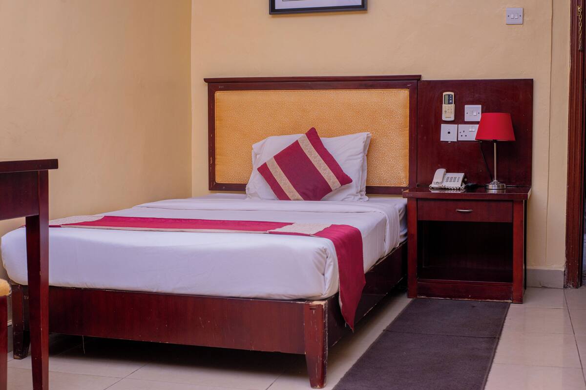 A hotel room with a wooden bed, a bedside table with a lamp, and a telephone.