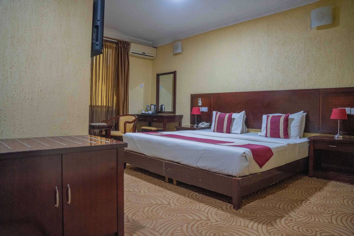 A hotel room with a large bed, a desk, a chair, a wardrobe, and a mirror.