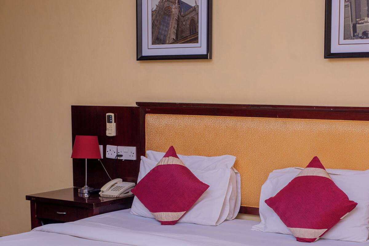 A hotel room with a large bed, two bedside tables, a nightstand, a telephone, and two framed pictures on the wall.