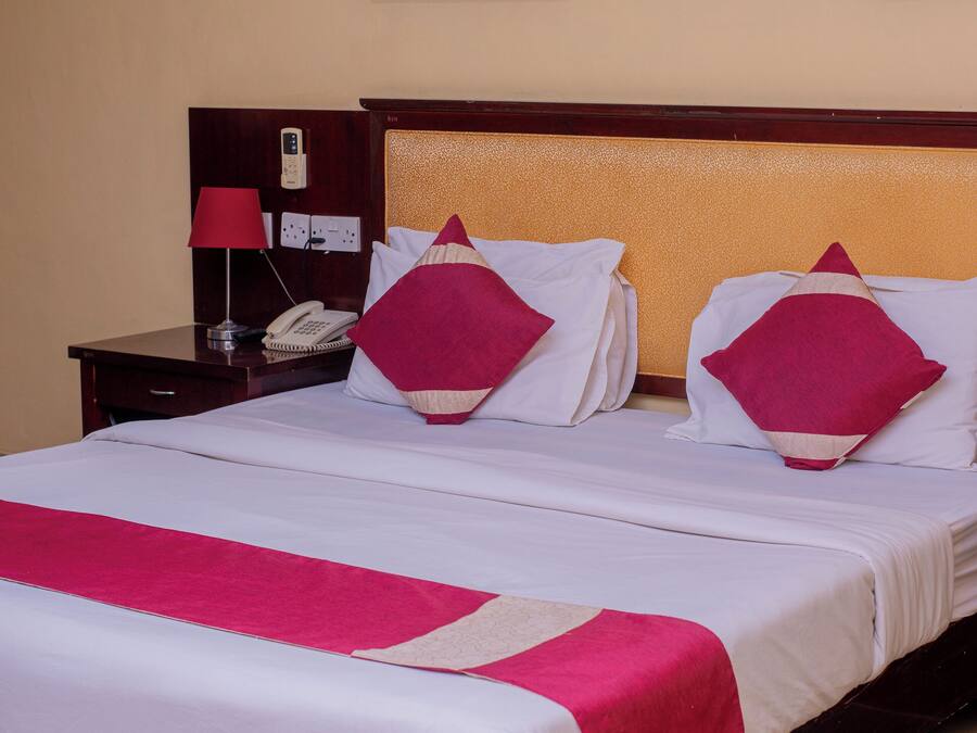 Quarto de hotel com uma cama grande, duas mesas de cabeceira, um criado-mudo, um telefone e duas fotografias emolduradas na parede.