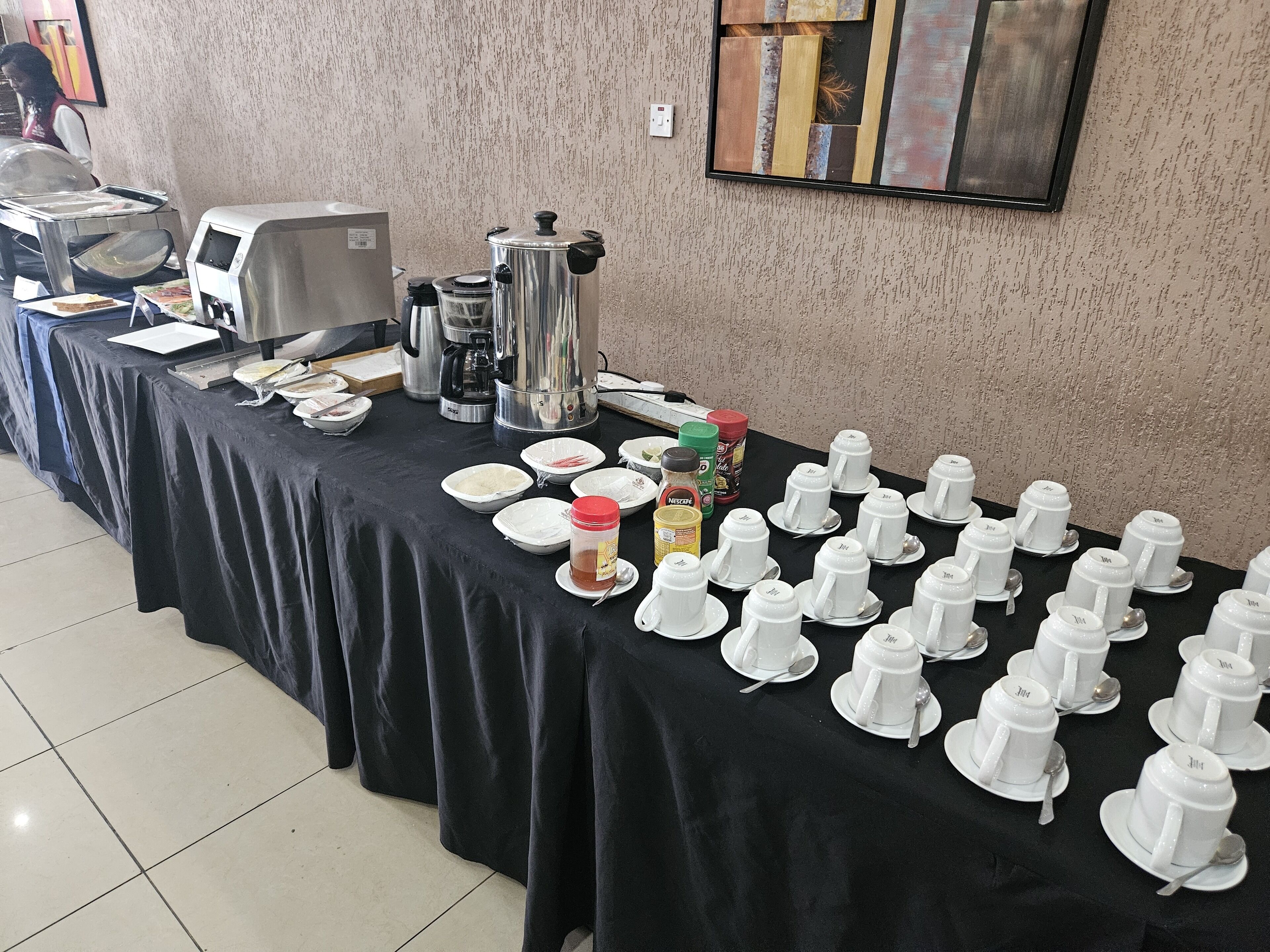 A buffet setup with multiple coffee machines, a variety of food items, and numerous white cups and saucers arranged on a table.