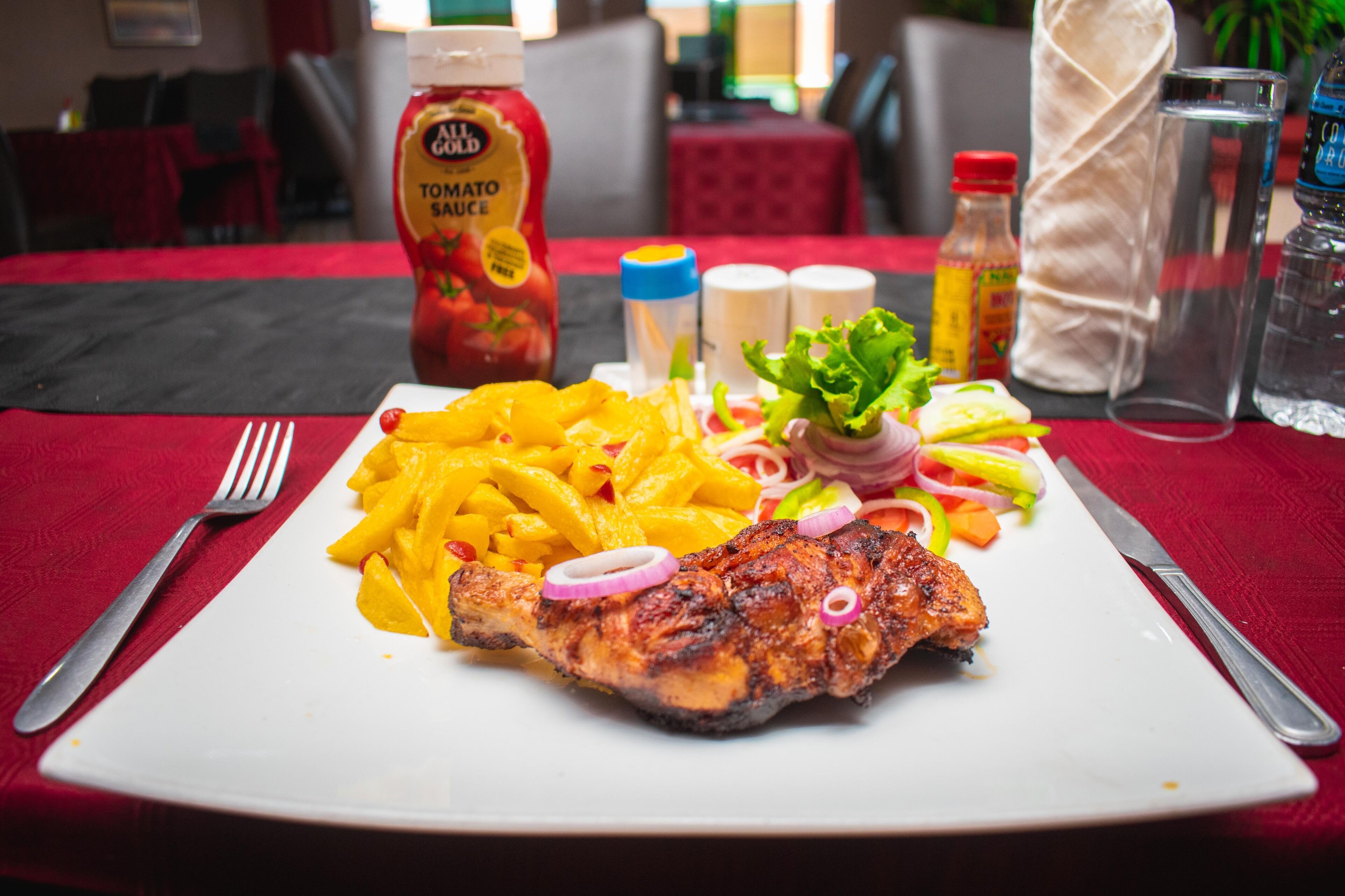 Ein Teller mit gegrilltem Fleisch, Pommes und Gemüse auf einer roten Tischdecke.